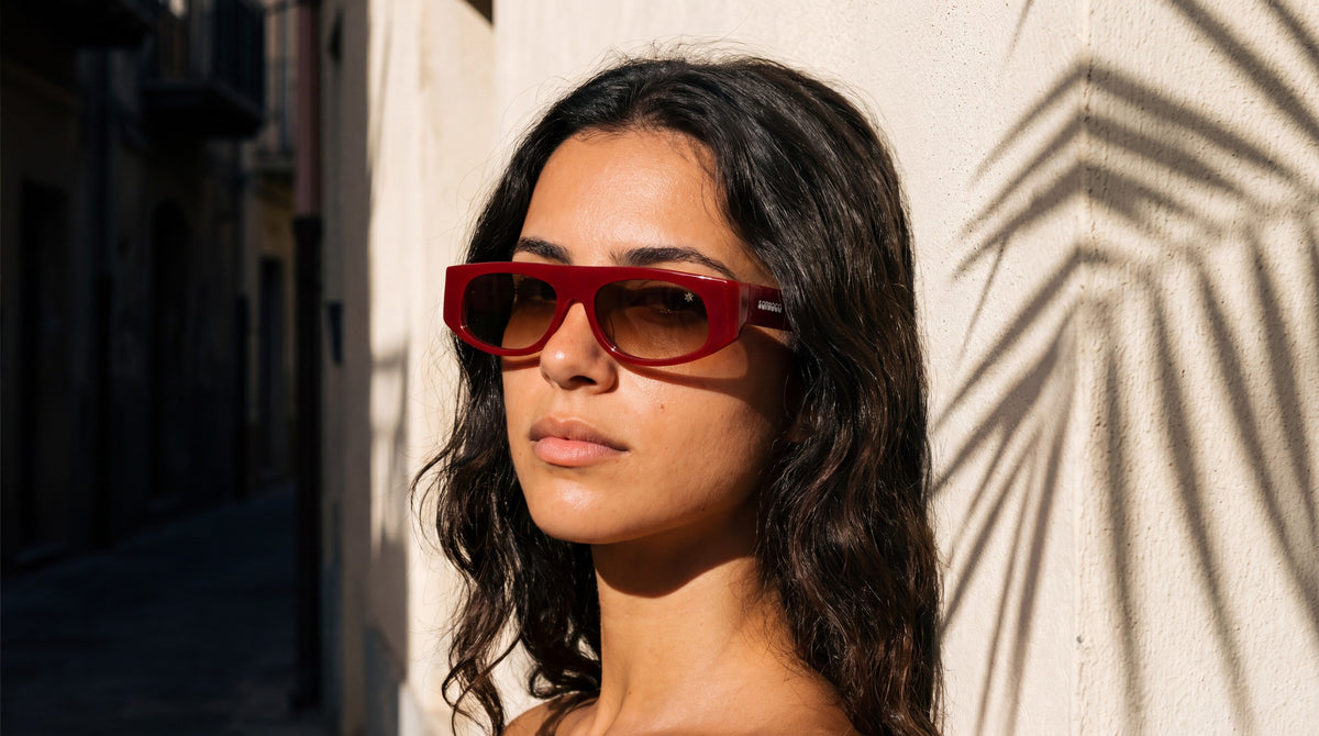 Donna con occhiali da sole Scirocco ESTESIA RED appoggiata a un muro in un vicolo siciliano